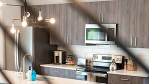 A modern kitchen with a central island, bar stools, a microwave, and a stove.