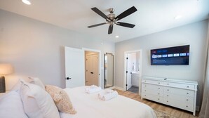 A modern hotel room with a bed, a ceiling fan, a TV mounted on the wall, and a white dresser.