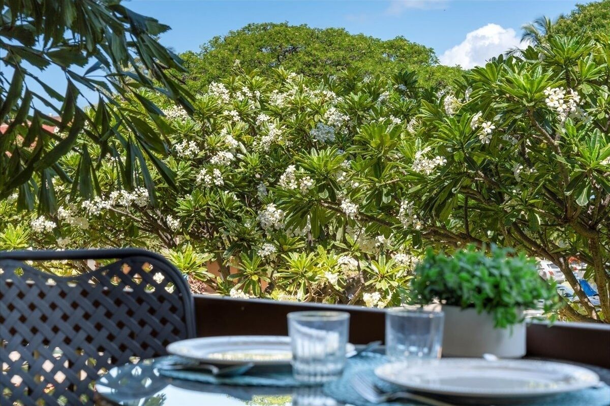 An outdoor dining area with a table set for two, surrounded by lush greenery and flowering plants.