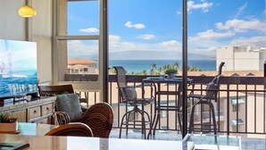 Un balcone con vista sull'oceano, una zona pranzo con sedie, una televisione e un tavolo con una pianta.