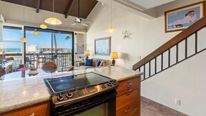 Una cucina con piano cottura integrato, zona pranzo con sedie e tavolo, e vista sull'oceano attraverso ampie finestre.