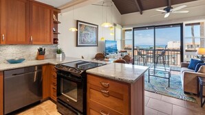 Una cucina moderna con mobili in legno, forno integrato e un'isola grande. C'è una zona pranzo con vista sull'oceano.