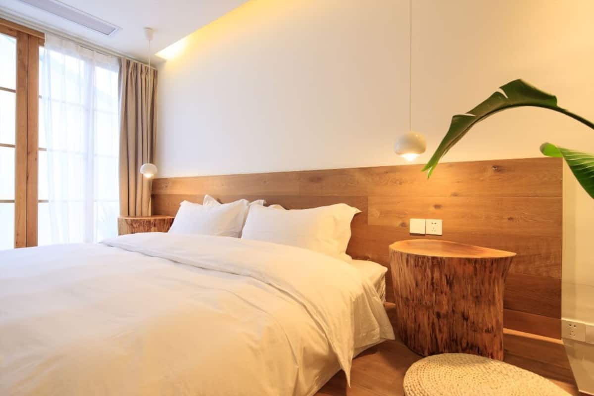 Une chambre moderne avec un grand lit, une tête de lit en bois et une table de chevet ronde en bois.