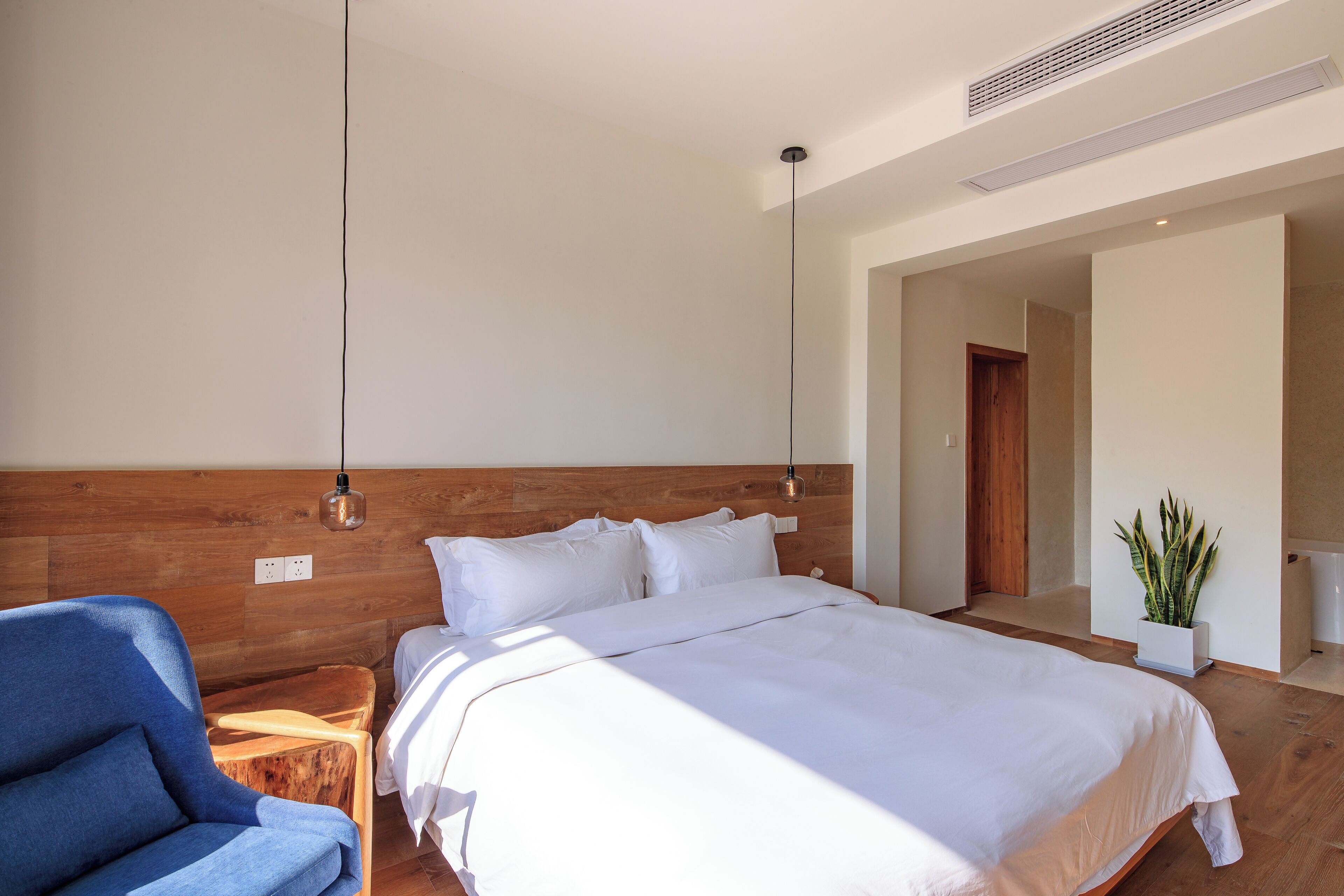 A modern bedroom with a large bed, a blue chair, and a potted plant.
