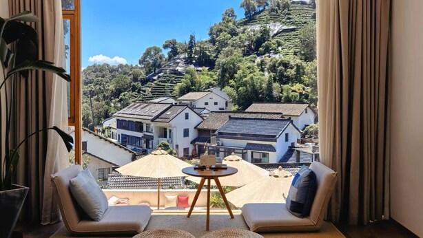Ein Zimmer mit Blick auf traditionelle Häuser an einem Hügel, inklusive einer Couch, einem kleinen Tisch und einem Blumentopf.