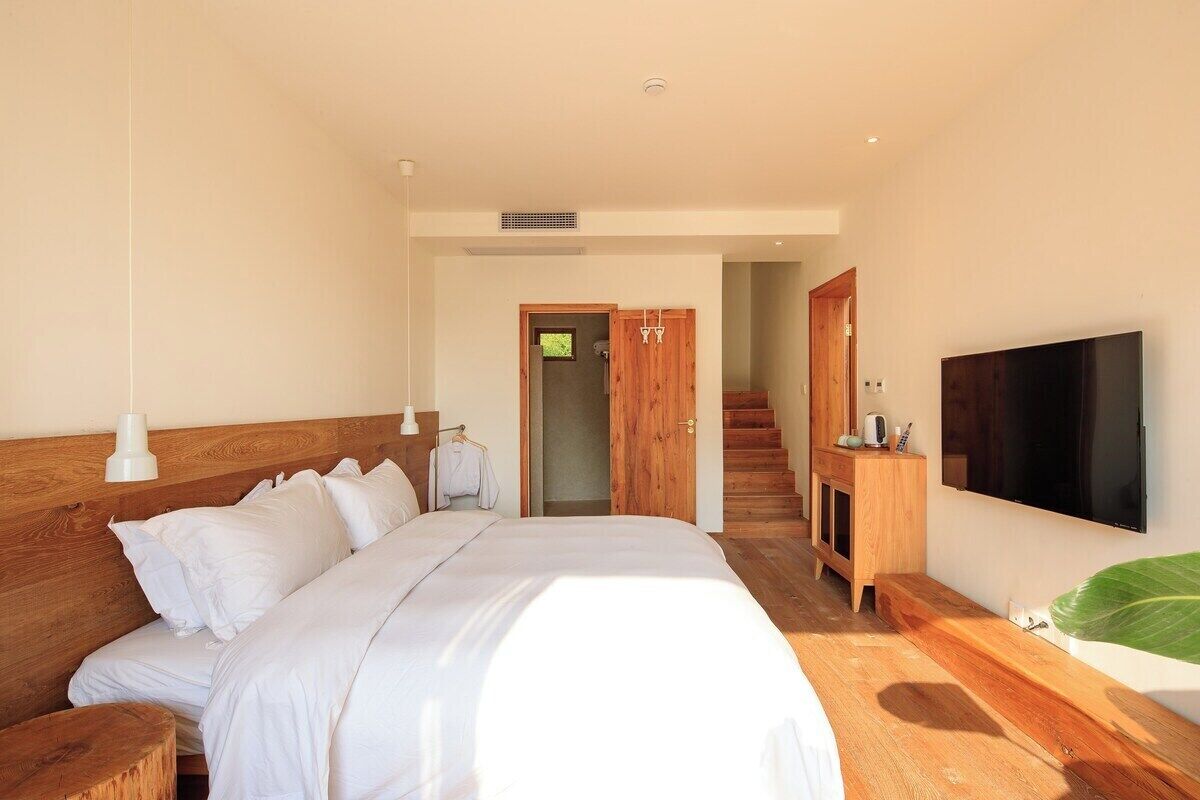 Une chambre dotée d’un grand lit, d’une tête de lit en bois, d’un téléviseur fixé au mur et d’un escalier menant à l’étage supérieur.