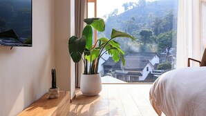Ein Schlafzimmer mit großem Fenster, Topfblume und Bett.