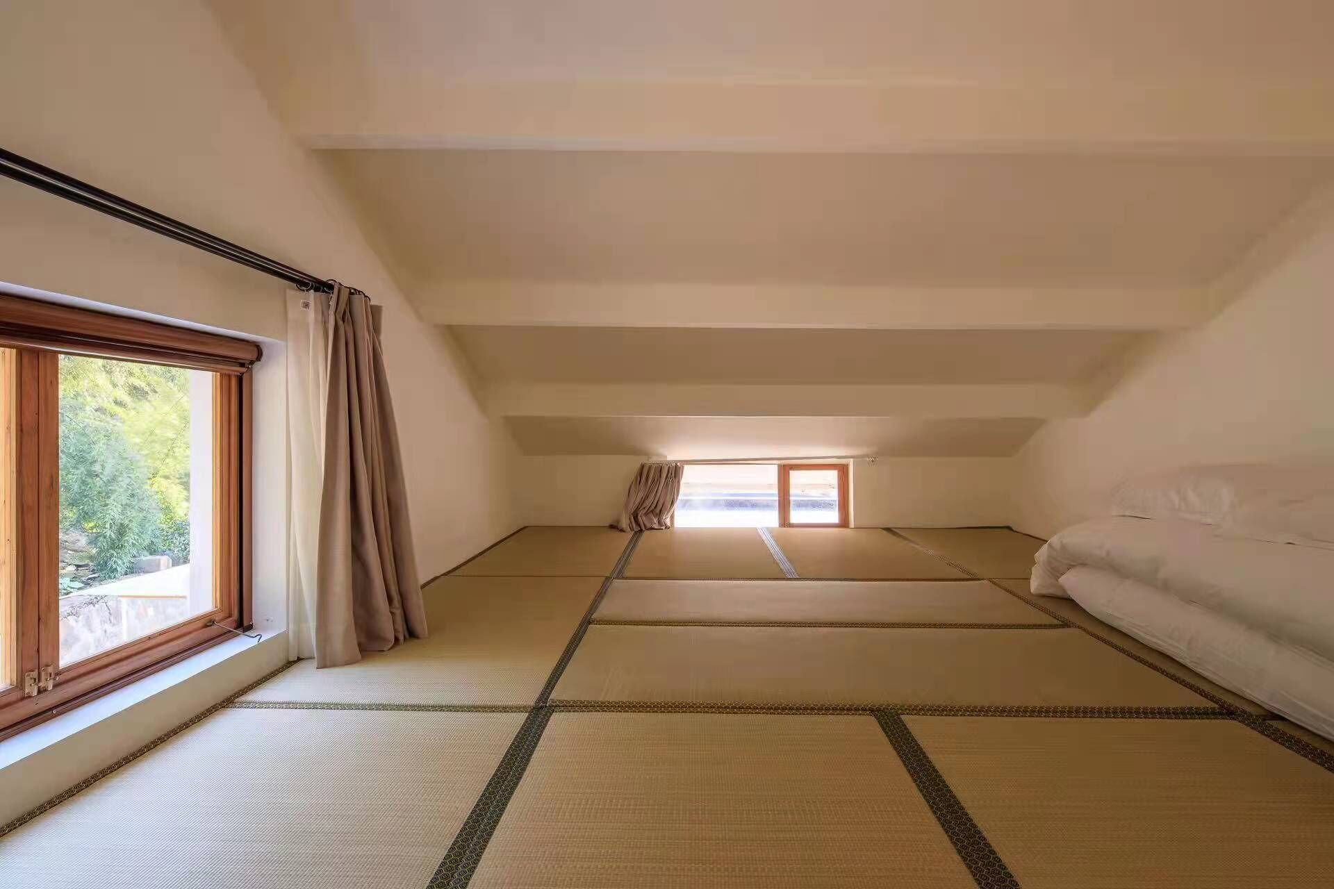 A room with tatami flooring, a low ceiling, and a large window on the left.