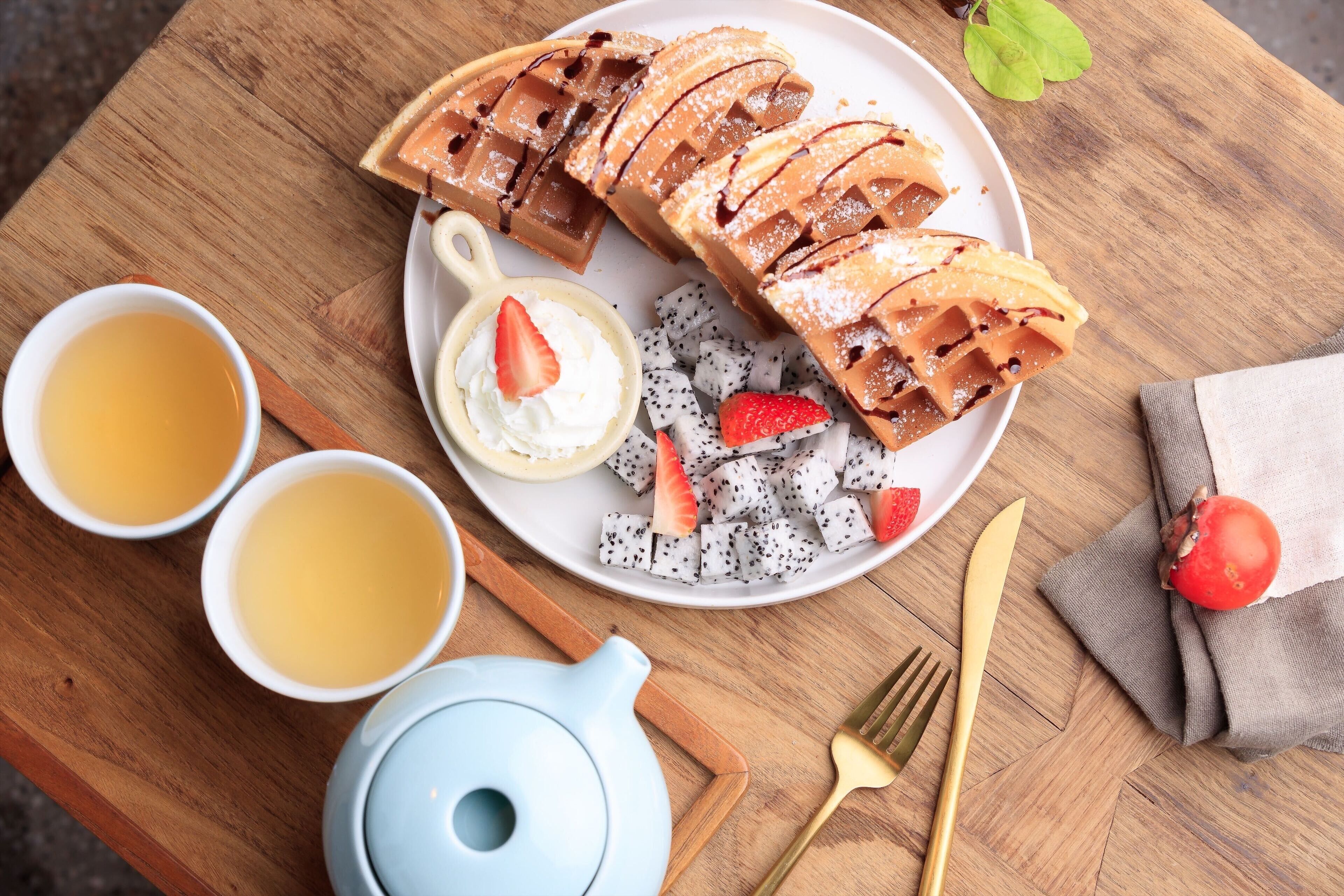 A breakfast setting with waffles, fruit, and tea on a wooden table.