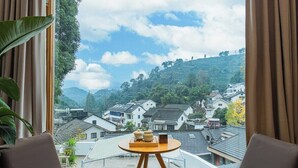 Ein Zimmer mit Blick auf terrassenartige Häuser und Hügel. Ein runder Holztisch mit Tablett und einer kleinen Pflanze ist vorhanden.