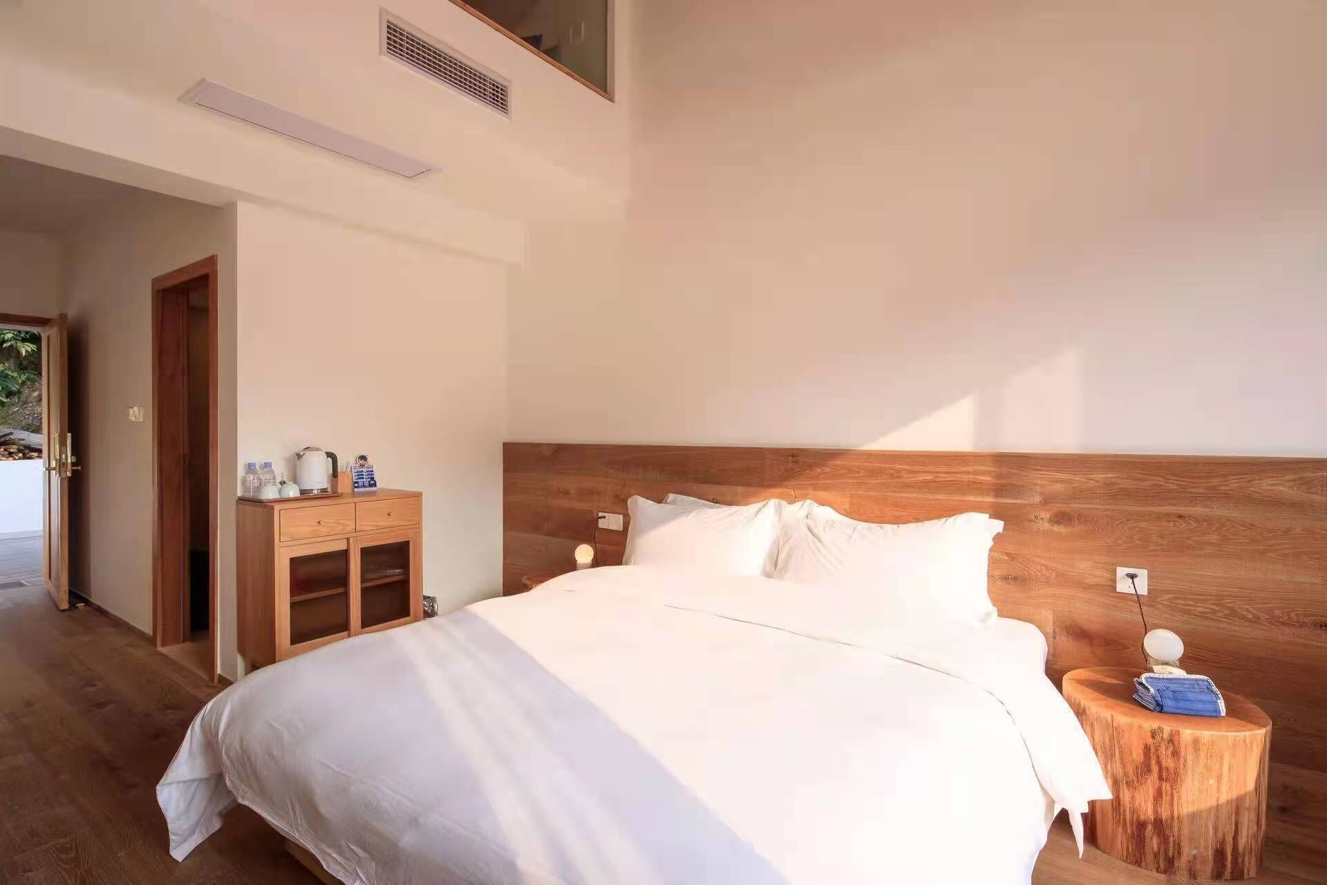 A bedroom with a wooden headboard, a wooden nightstand with a lamp, and a wooden wardrobe.