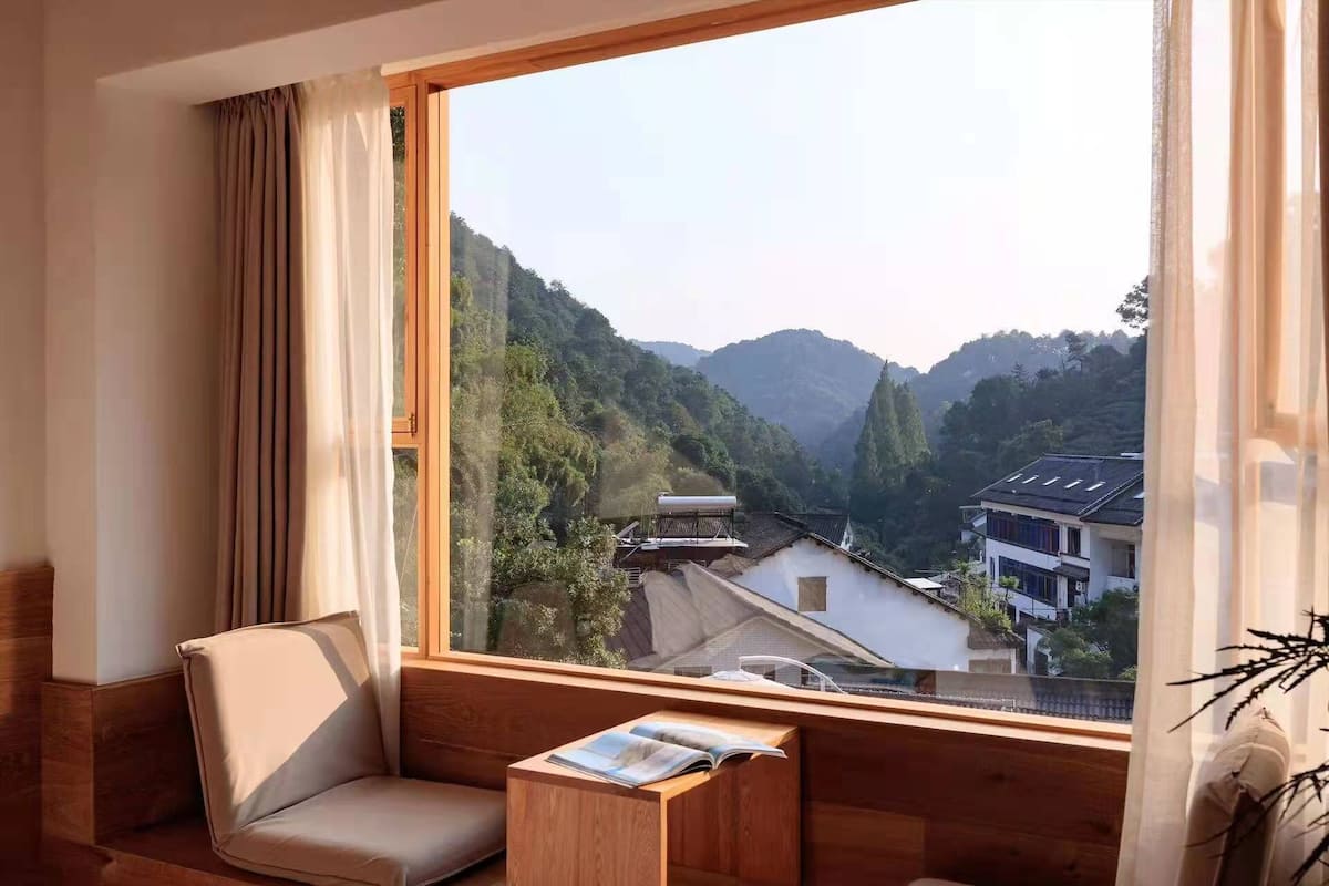 Une pièce dotée d’une grande fenêtre donnant sur un paysage montagneux et des bâtiments traditionnels.