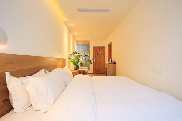 A neatly made bed with white linens and pillows, a wooden headboard, and a small bedside table with a plant.