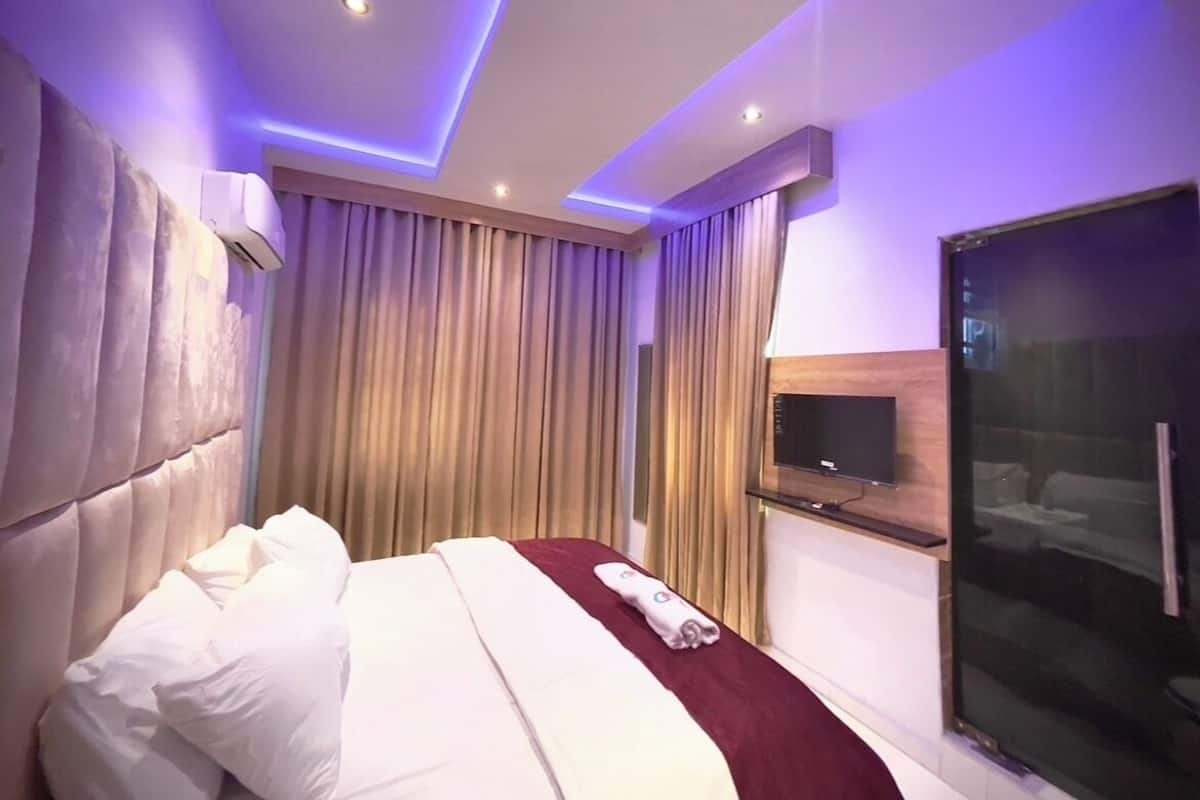 Ein Hotelzimmer mit Bett, Vorhängen, einer Klimaanlage, einem Fernseher und einer Glastrennwand.