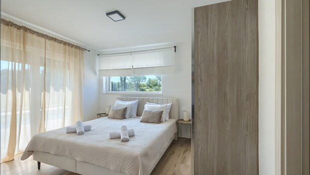 Ein Schlafzimmer mit einem großen Bett, einem Fenster mit Vorhängen, einem Nachttisch und einer Holztür.