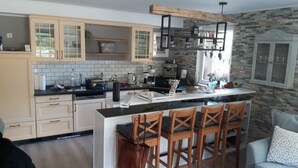 Eine moderne Küche mit weißen Schränken, einer schwarzen Arbeitsplatte und einer Steinwand. Es gibt eine Bar mit Holzstühlen und einer Kaffeemaschine.
