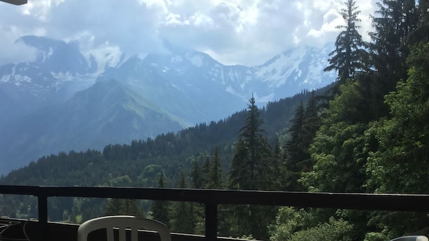Ein Balkon mit Tisch und zwei Stühlen, mit Blick auf eine gebirgige Landschaft mit dichtem Wald.