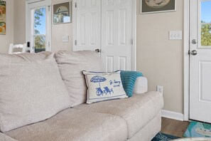 A beige sofa with a cushion featuring a beach scene, a white door, and a small rug. - The Floridian, Old Florida Charm with Modern Comfort (Saint George Island)