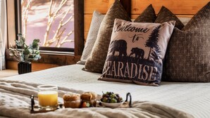 A bed with a 'Welcome to Paradise' pillow, a glass of orange juice, muffins, and a bowl of berries.