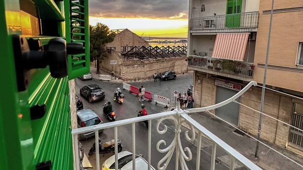 A balcony with a view of a street, buildings, and a sunset.