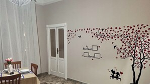 A dining area with a table set for two, a red sofa, and a wall with a tree decal and heart shapes.