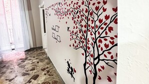 A hallway with a stone floor, a wall mural of a tree with red leaves, and a door with a heart-shaped decoration.