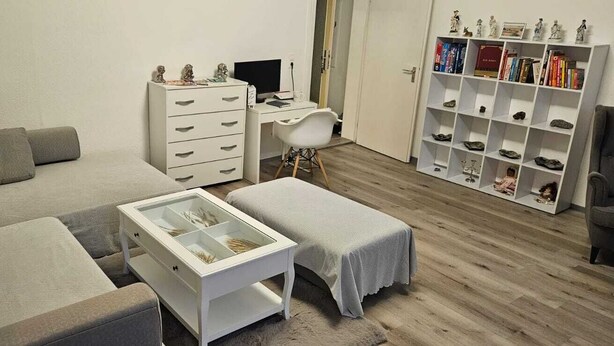 A modern living room with a grey sofa, a white coffee table, a white desk with a computer, and a shoe display unit. - "charmante 2 Zimmer Wohnung in Ansbach" (Ansbach)