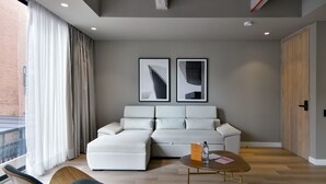 Ein modernes Wohnzimmer mit einem weißen Sofa, einem Holztisch und Blick auf ein Backsteingebäude durch große Fenster.