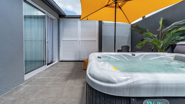 Un espace moderne aménagé à l’extérieur avec un jacuzzi, un parasol jaune, une porte-fenêtre coulissante et un pot de fleurs.