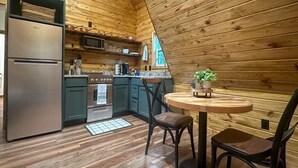 A kitchen with wooden walls, a refrigerator, stove, microwave, and a dining table with chairs.