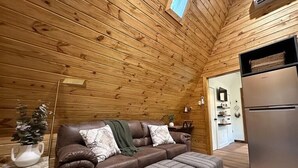A cozy room with wooden walls, a brown leather sofa, a small table with a plant, and a refrigerator.