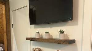 A wall-mounted TV above three wooden shelves, each holding decorative items.