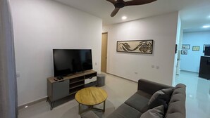 A modern living room with a flat-screen TV, a ceiling fan, a sofa, and a small wooden table.