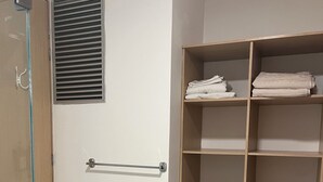 A walk-in closet with wooden shelving, a towel rack, and a glass shower door.