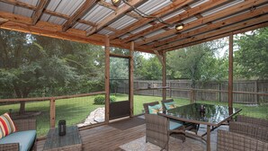 A covered patio with a glass table and wicker furniture, overlooking a backyard with a wooden fence and trees. - ~ 3 miles to Kyle Field/TAMU ~ 8 min to Santa’s Wonderland ~  (College Station)