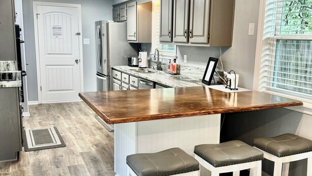A kitchen with a wooden island, bar stools, and a view of the outdoors through a window. - ~ 3 miles to Kyle Field/TAMU ~ 8 min to Santa’s Wonderland ~  (College Station)