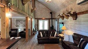 Un interior rústico con techo de madera, ciervos disecados en la pared, un sofá de cuero y una mesa de centro de madera.