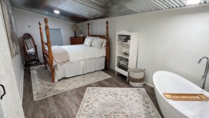 Un dormitorio con una cama grande, un armario de madera, una bañera blanca y una alfombra estampada.