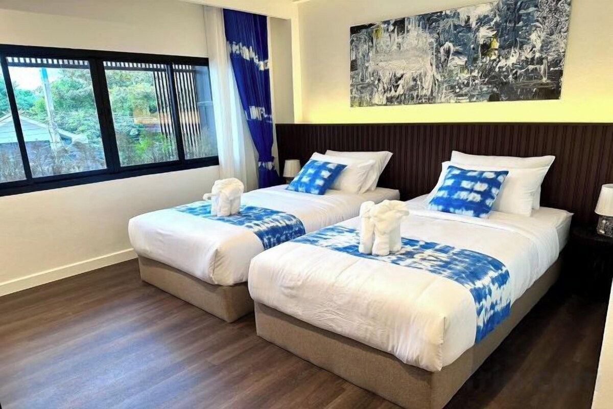 Habitación de hotel con dos camas, un ventanal grande y un cuadro en la pared.
