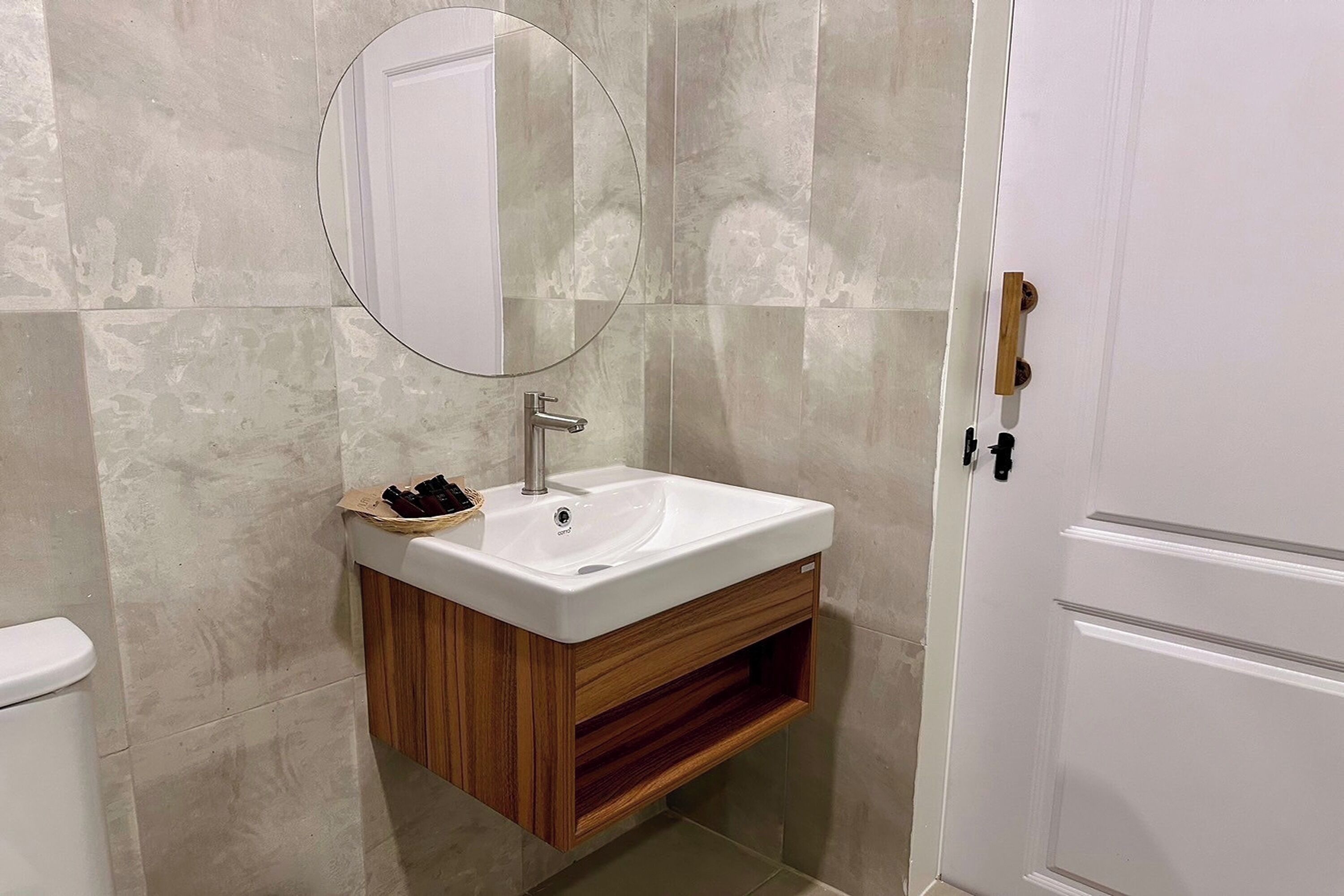A bathroom with a white sink, wooden vanity, and a round mirror.