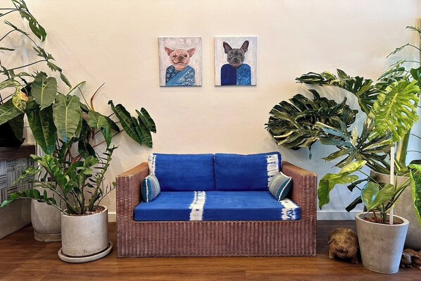 Un sofá azul con cojines de diseño blanco y azul, rodeado de grandes macetas con plantas.