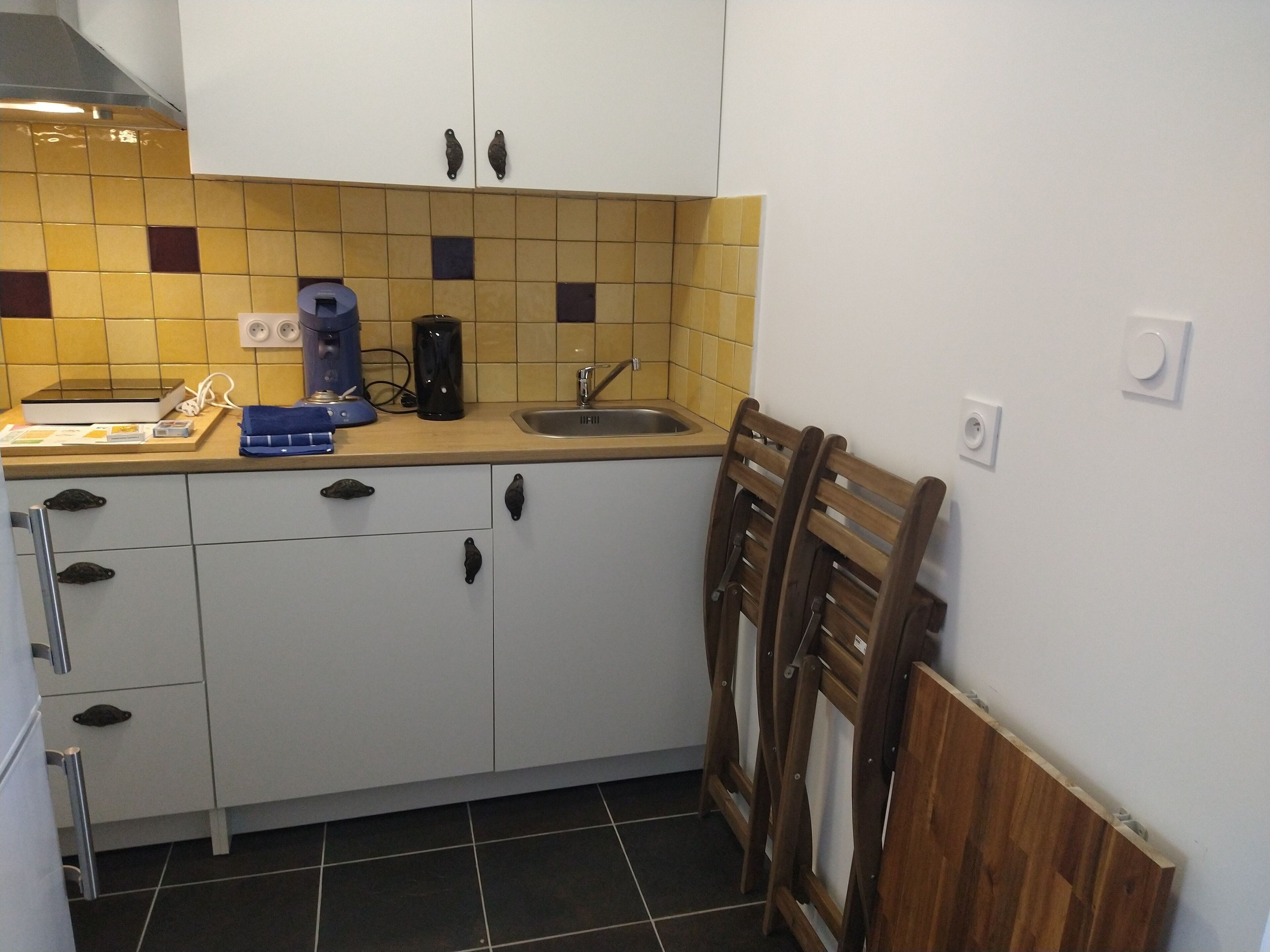 Eine kleine Küche mit weißen Schränken, einer gefliesten Spritzschutzwand, einem Waschbecken und einer Kaffeemaschine.