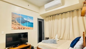 A bedroom with a bed, a TV, an air conditioner, and a wall-mounted artwork. - Mactan cozy 1 bedroom with 3 beds (Lapu-Lapu)