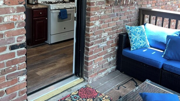 Fachada de ladrillo con puerta de vidrio que da a una zona de cocina, un sofá azul con cojines y un felpudo estampado.
