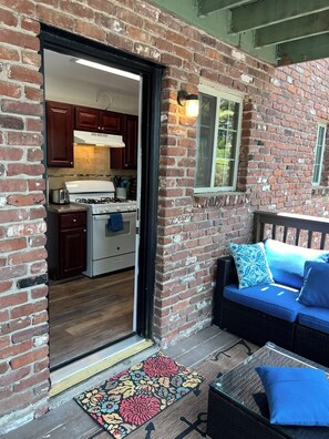 Fachada de ladrillo con puerta de vidrio que da a una zona de cocina, un sofá azul con cojines y un felpudo estampado.