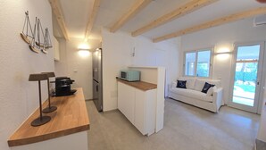 A modern kitchen with a built-in microwave, a coffee machine, and a wooden countertop. There is a white sofa with decorative pillows and a window with a view of the outdoors. - Renovated Villa | Pool | Beach 300m Walk | 4 Guests | Pula Sardinia (Santa Margherita di Pula)