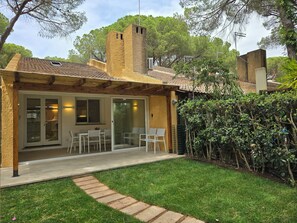 A covered patio with a seating area, a brick chimney, and a view of the surrounding trees.