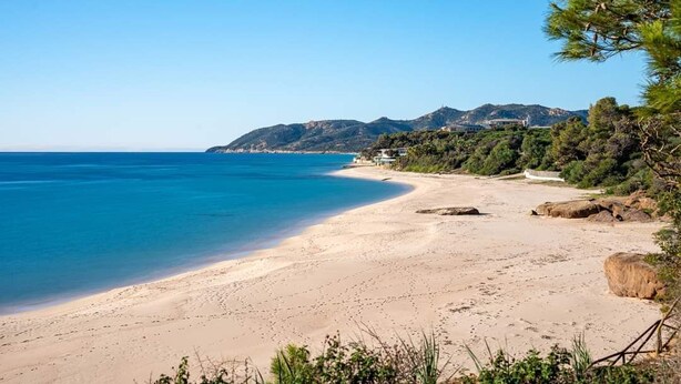 A beach with clear blue water, sandy shore, and a mountainous backdrop. - Renovated Villa | Pool | Beach 300m Walk | 4 Guests | Pula Sardinia (Santa Margherita di Pula)