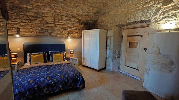 Une chambre avec un plafond en pierre, un lit recouvert d’une literie à motifs, une armoire blanche et une porte en bois.