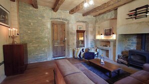 Ein rustikaler Raum mit Steinwänden, Holzbalken, einem Kamin, einer Couch und einem Tisch.
